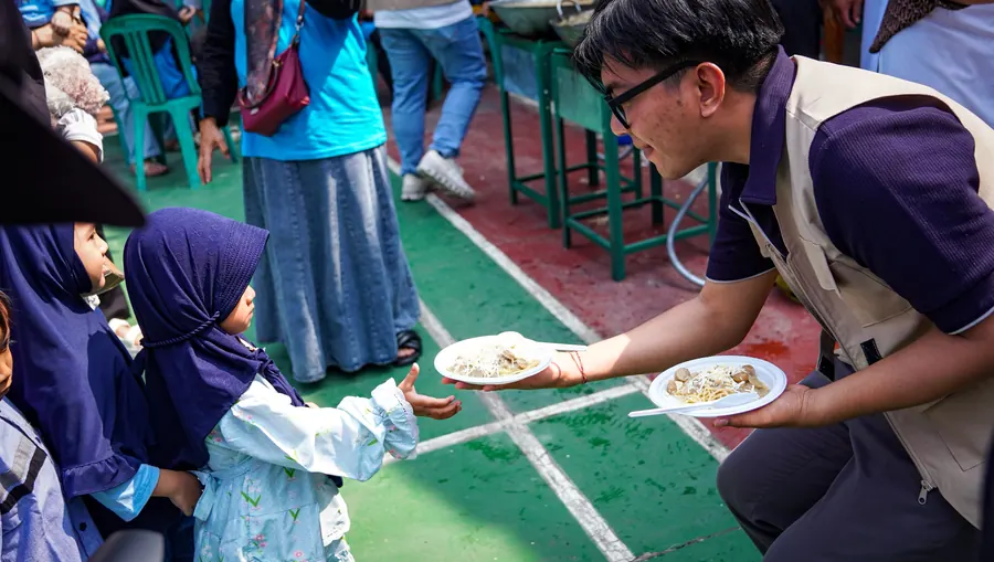 Relawan memberikan piring makanan kepada anak